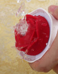 Hand holding the Nectar rose vibrator in its white cup-shaped body while water flows over the red petals and central opening