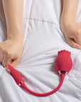 Pink Mermaid rose suction vibrator on white bedding with a person holding the petal-shaped connected egg, showing the flexible U-shaped cord and two body buttons