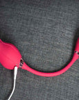 Rear view of the pink Mermaid rose suction vibrator with a white magnetic charging cable beside the metallic neck trim and the connected petal-shaped egg