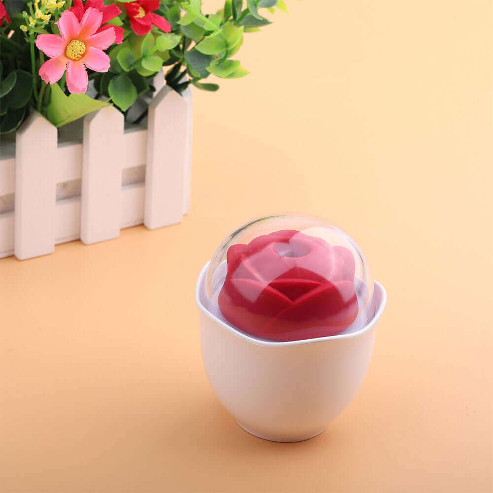 Red Nectar rose vibrator and white holder under a clear dome cover, pictured on a peach surface beside decorative flowers