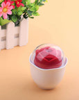 Red Nectar rose vibrator and white holder under a clear dome cover, pictured on a peach surface beside decorative flowers