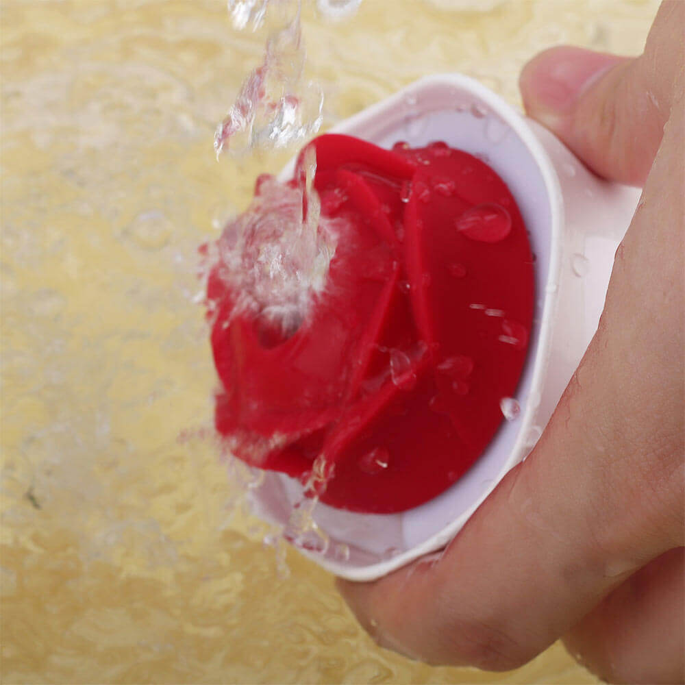 Hand holding the Nectar rose vibrator in its white cup-shaped body while water flows over the red petals and central opening