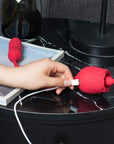 Hand attaching a white magnetic USB cable to the two charging contacts on the red Rhea rose head, with the connected ribbed end behind it