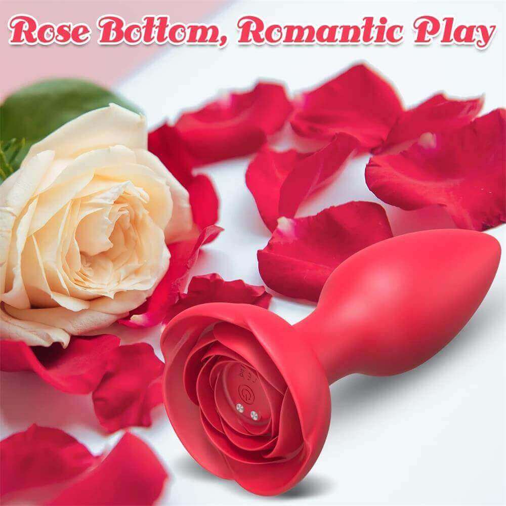 Red rose vibrating plug resting among rose petals with its wide flower base, underside power button and two magnetic charging contacts facing forward