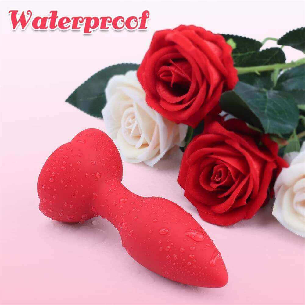 Red rose vibrating plug with water droplets on its smooth tapered bud and petal base beside decorative red and white roses