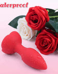 Red rose vibrating plug with water droplets on its smooth tapered bud and petal base beside decorative red and white roses