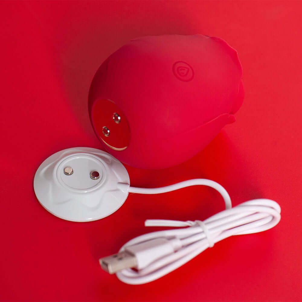 Red rose tapping stimulator showing two underside contacts beside its white round magnetic USB charging dock