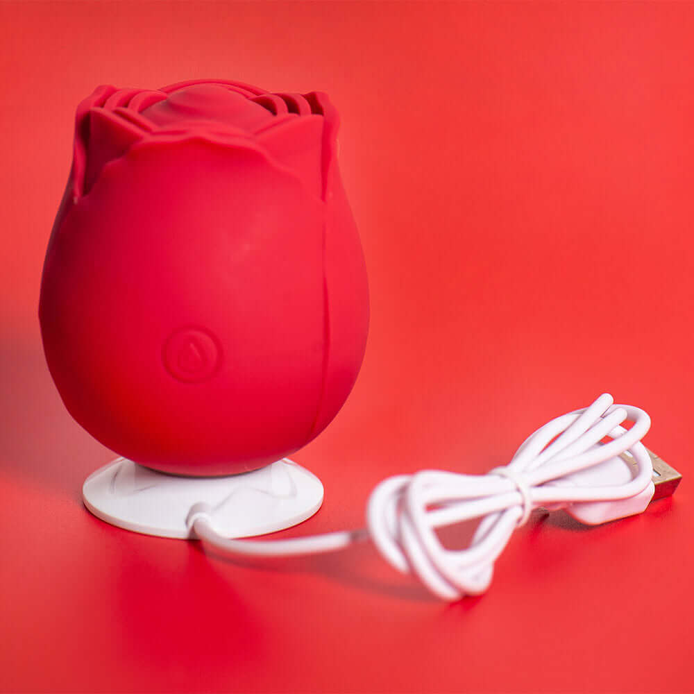 Red rose tapping stimulator standing on its white round charging dock with the USB cable coiled beside it