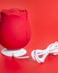 Red rose tapping stimulator standing on its white round charging dock with the USB cable coiled beside it