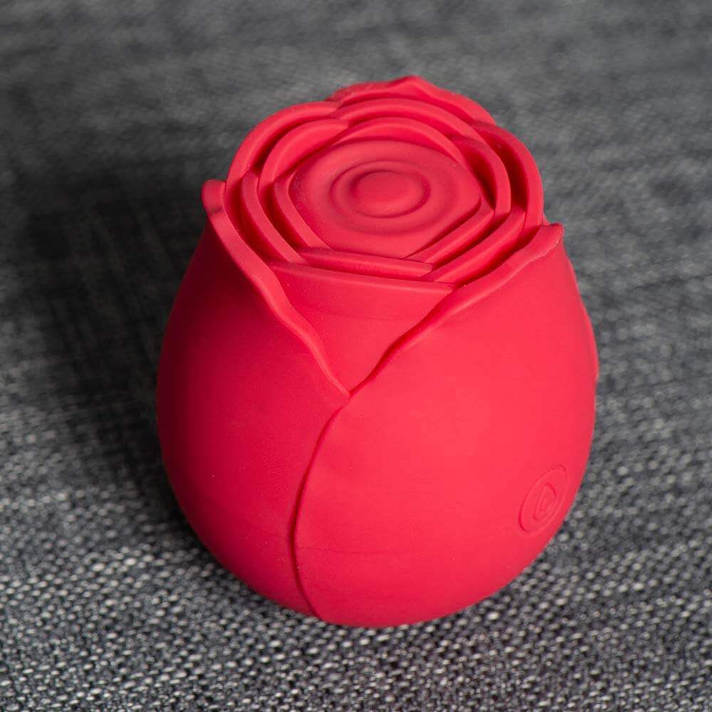 Angled Red rose tapping stimulator on grey fabric showing the concentric central pad, layered petals and single button