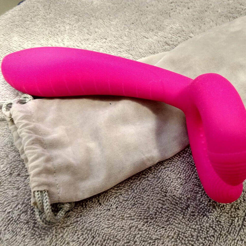 Side photograph of the Pink Y-1 vibrator showing its curved split head and textured long body resting on a fabric pouch